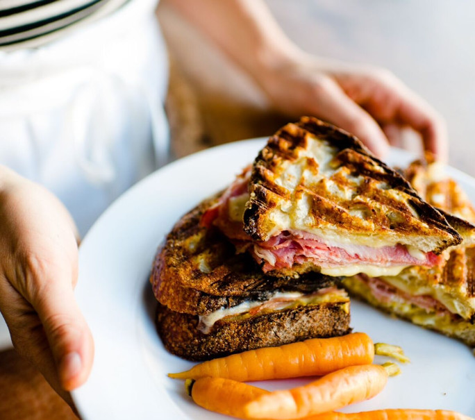 An expertly toasted ham and cheese sandwich with a side of carrots