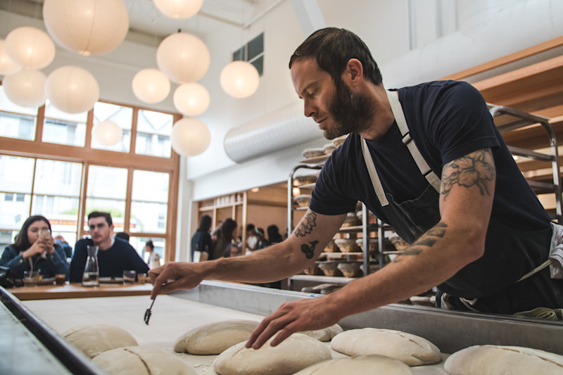 Chad, one of our bakers, uses a lame tool to score loaves of bread before they go into the oven