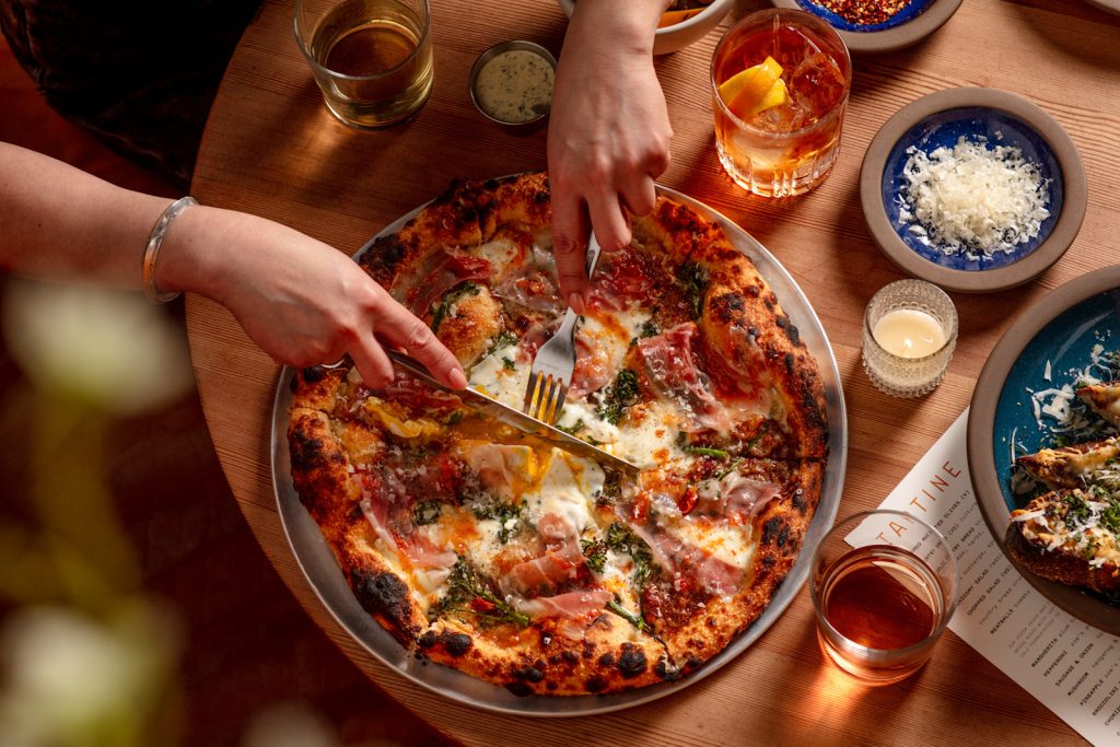 A customer cutting into one of our delicious Manufactory pizzas